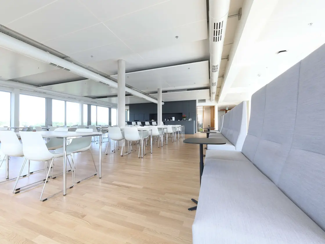 sutter-medizintechnik-grosser-sozialraum-© Kiefer und Sohn GmbH.jpg Heller, moderner Sozialraum bei Sutter Medizintechnik mit langen grauen Sitzbänken, weißen Stühlen, Tischen und großer Fensterfront.