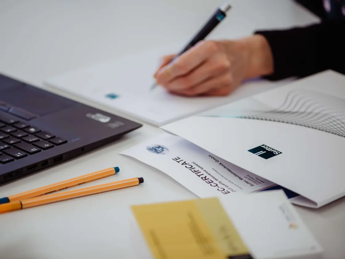 sutter-bewerbung-karriere-schreibtisch.jpg Nahaufnahme eines Schreibtisches mit Laptop, Bewerbungsunterlagen und Hand beim Schreiben – Symbolbild für den Bewerbungsprozess bei Sutter Medizintechnik