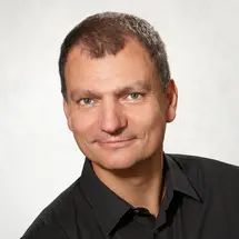 Dr. Oestreicher mit kurzem Haar und schwarzem Hemd vor hellem Hintergrund