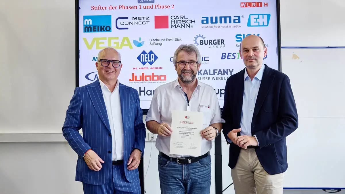 sutter-robotiktag-urkundenübergabe-2025.jpg Drei Männer bei einer Urkundenübergabe vor einer Sponsorenwand am Robotiktag 2025; ein Vertreter von Sutter Medizintechnik hält die Urkunde der Hochschule Offenburg.