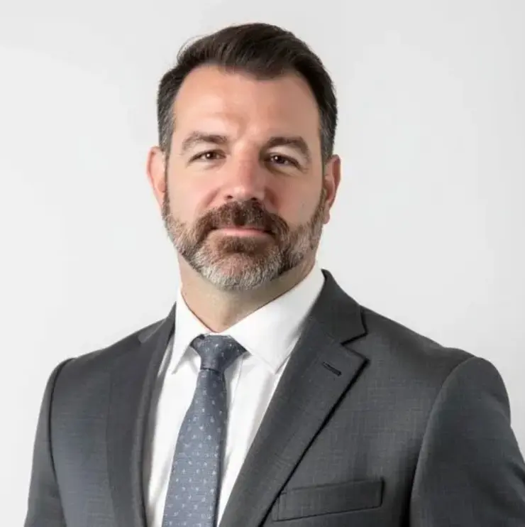 Person in dark grey suit with white shirt and dotted tie – professional appearance in a medical or corporate setting.