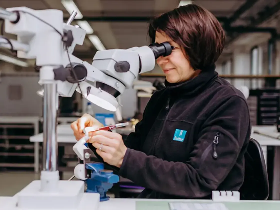 sutter-mitarbeiterin-montage-mikroskop.jpg Mitarbeiterin von Sutter Medizintechnik arbeitet hochkonzentriert unter dem Mikroskop in der präzisen Montage von medizinischen Instrumenten